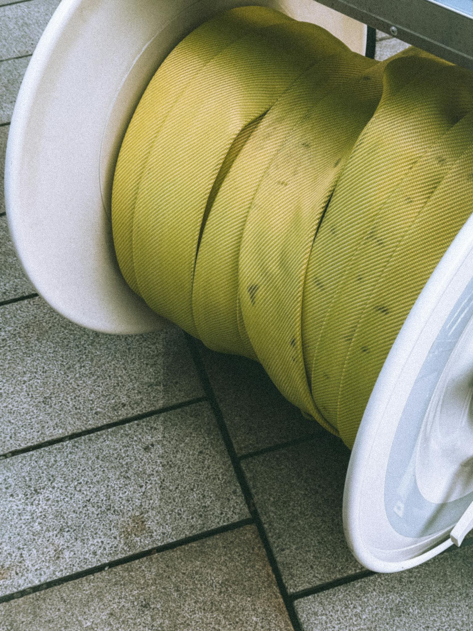 Detailed view of a yellow industrial hose reel on a tiled pavement in an outdoor setting.